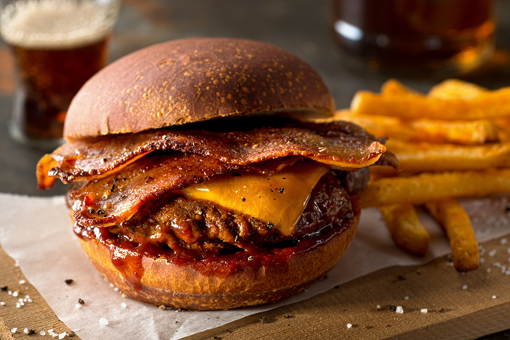 A delicious pub style bacon cheeseburger with barbecue sauce and french fries.
