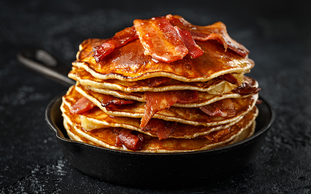 Pancakes with crispy bacon and maple syrup in cast iron skillet, frying pan. Morning Breakfast.